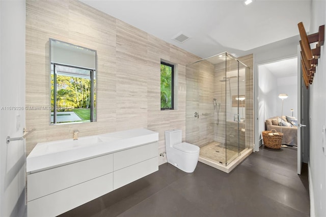 bathroom with a tile shower, vanity, toilet, and tile walls