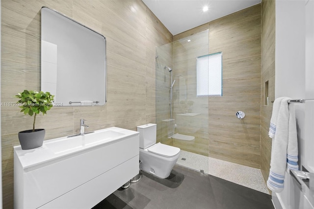 bathroom with a tile shower, vanity, toilet, and tile walls