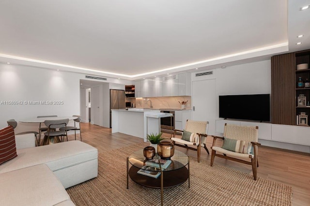 living room featuring light wood-type flooring, sink, and a tray ceiling