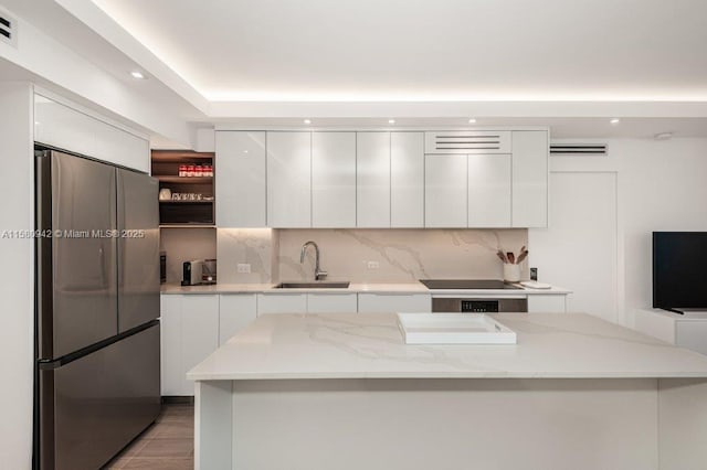 kitchen featuring black electric stovetop, sink, light stone countertops, white cabinets, and stainless steel fridge