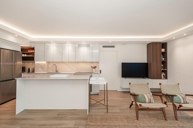 kitchen featuring white cabinets, sink, stainless steel refrigerator, and a center island