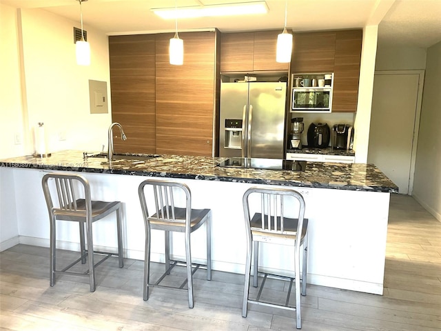 kitchen with sink, stainless steel fridge, kitchen peninsula, light hardwood / wood-style flooring, and dark stone countertops