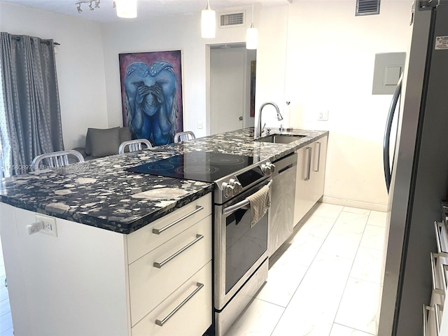 kitchen with decorative light fixtures, fridge, sink, stainless steel electric range oven, and an island with sink