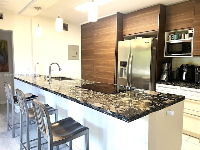 kitchen featuring sink, appliances with stainless steel finishes, dark stone counters, and a kitchen bar