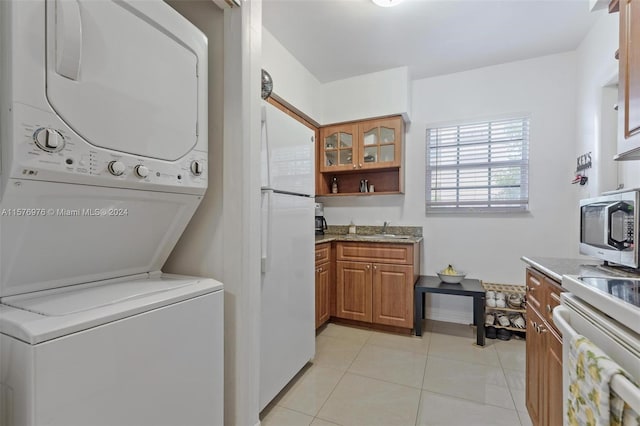 laundry area with sink, light tile floors, and stacked washer and clothes dryer