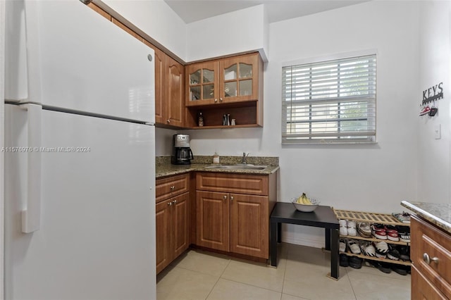 kitchen with sink, light tile flooring, white fridge, and dark stone counters