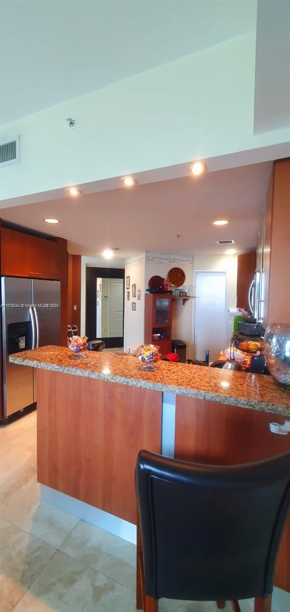 kitchen with stone counters, stainless steel refrigerator with ice dispenser, kitchen peninsula, and light tile flooring