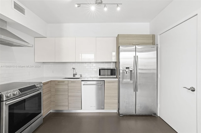 kitchen featuring appliances with stainless steel finishes, wall chimney exhaust hood, sink, white cabinets, and track lighting