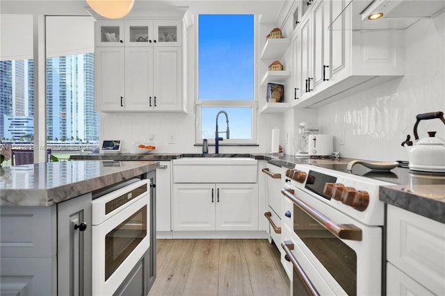 kitchen with double oven range, white cabinets, sink, stainless steel oven, and light wood-type flooring