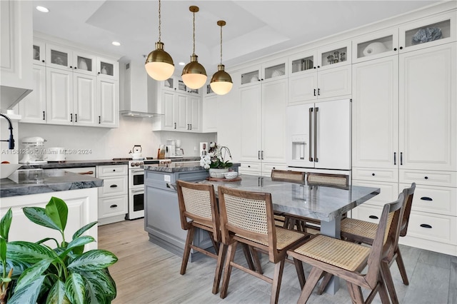 kitchen featuring light hardwood / wood-style floors, high end appliances, wall chimney range hood, a raised ceiling, and a center island