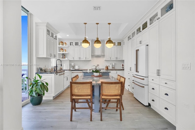 kitchen with a kitchen island, high end white fridge, white cabinetry, pendant lighting, and light wood-type flooring