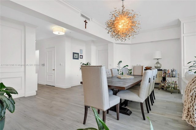 dining area with ornamental molding, an inviting chandelier, and light hardwood / wood-style floors