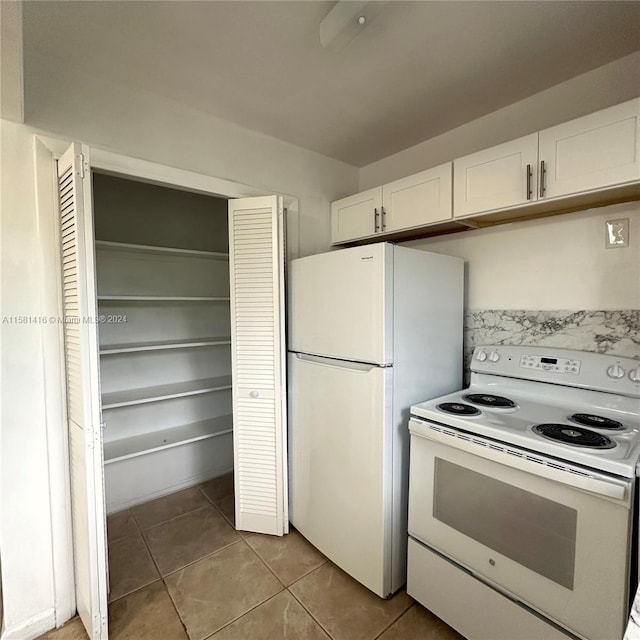 kitchen with white appliances, light tile patterned floors, and white cabinets