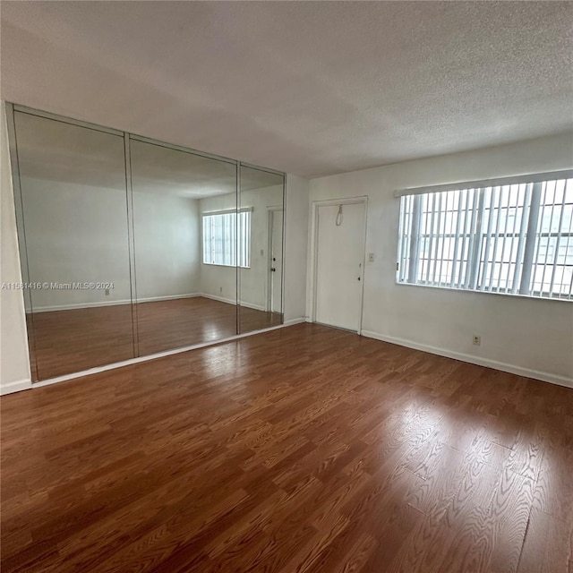 unfurnished bedroom featuring dark wood-type flooring, multiple windows, and a textured ceiling