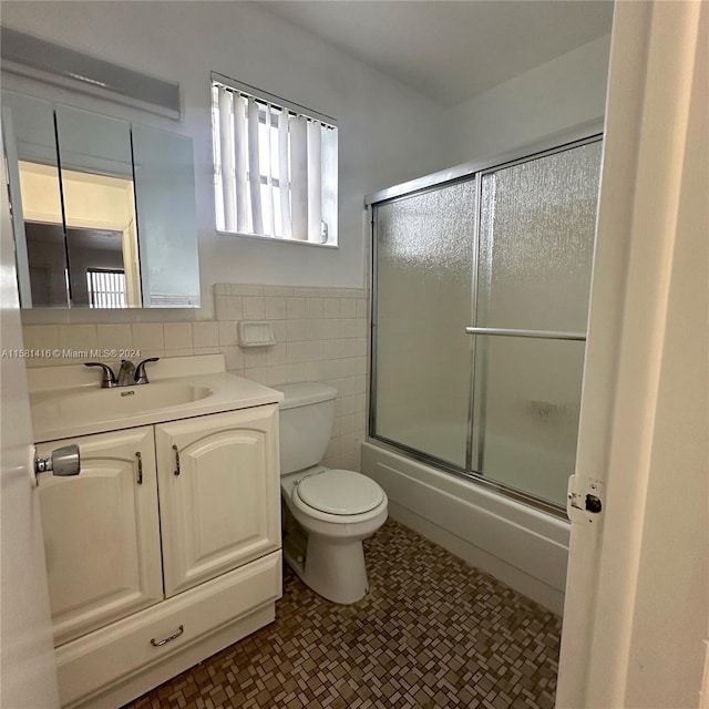 full bathroom featuring shower / bath combination with glass door, vanity, toilet, and tile walls