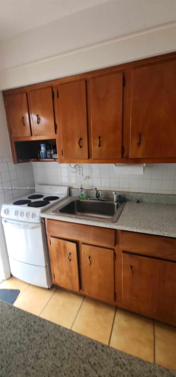 kitchen featuring light tile flooring, tasteful backsplash, sink, and white stove