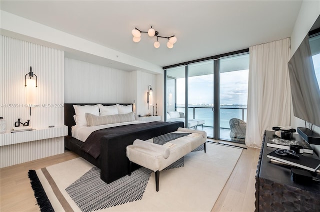 bedroom with a water view, a wall of windows, light hardwood / wood-style floors, and access to outside