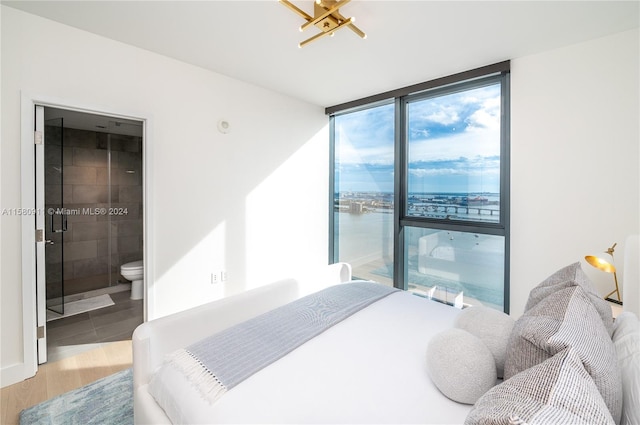 bedroom with ensuite bathroom, a water view, and tile floors