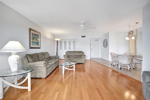 living room featuring ceiling fan with notable chandelier, a textured ceiling, and light hardwood / wood-style floors