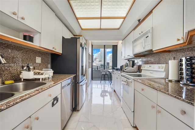 kitchen with backsplash, white appliances, sink, dark stone countertops, and white cabinetry