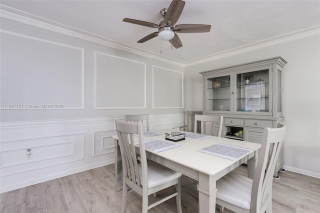 dining space featuring crown molding, light wood-style floors, a decorative wall, and a ceiling fan