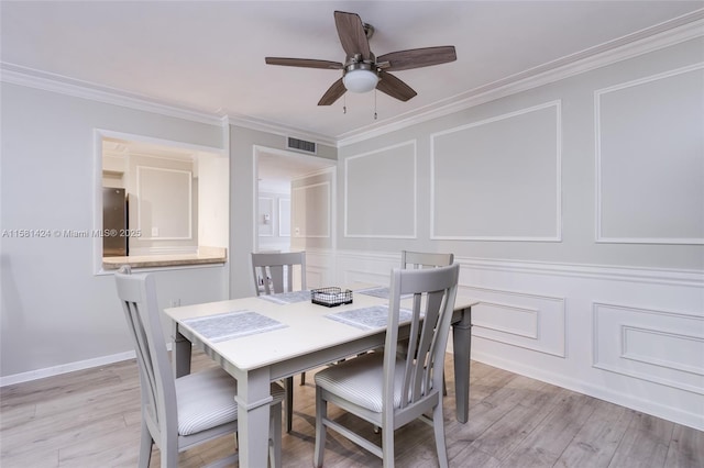 dining area with crown molding, light wood-style flooring, visible vents, and a decorative wall