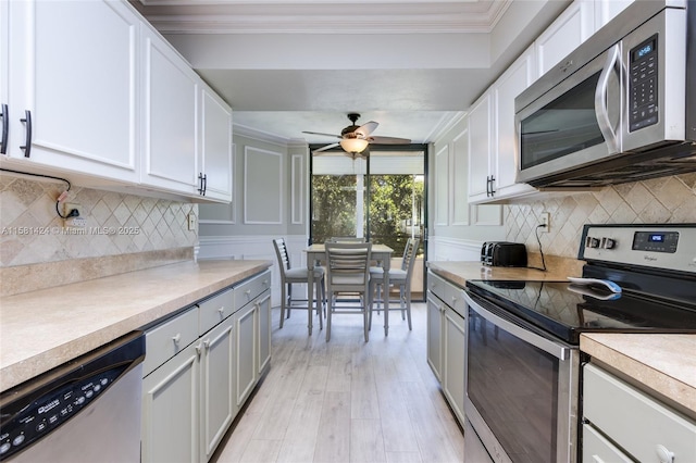 kitchen featuring stainless steel appliances, crown molding, decorative backsplash, and a ceiling fan