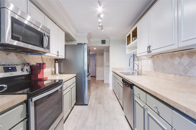 kitchen with a sink, light wood-style floors, light countertops, appliances with stainless steel finishes, and crown molding