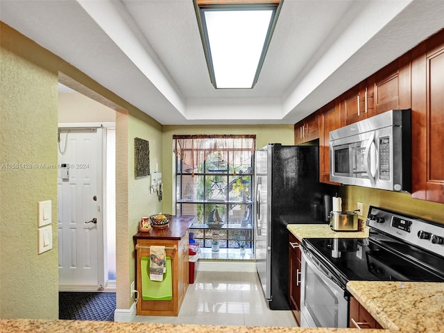 kitchen featuring stainless steel appliances, light stone countertops, a tray ceiling, and tile floors