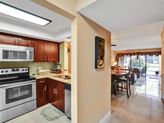 kitchen featuring stainless steel appliances, sink, light tile floors, and light stone counters