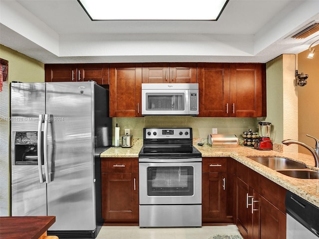 kitchen with a tray ceiling, sink, light stone countertops, and stainless steel appliances