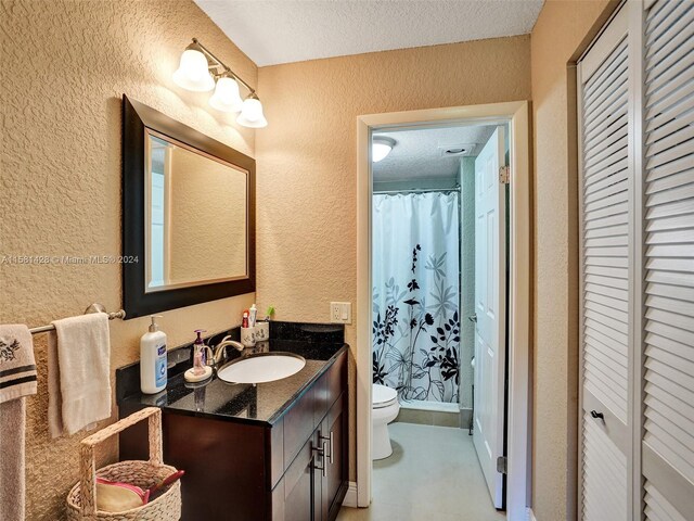 bathroom featuring vanity with extensive cabinet space, toilet, and a textured ceiling