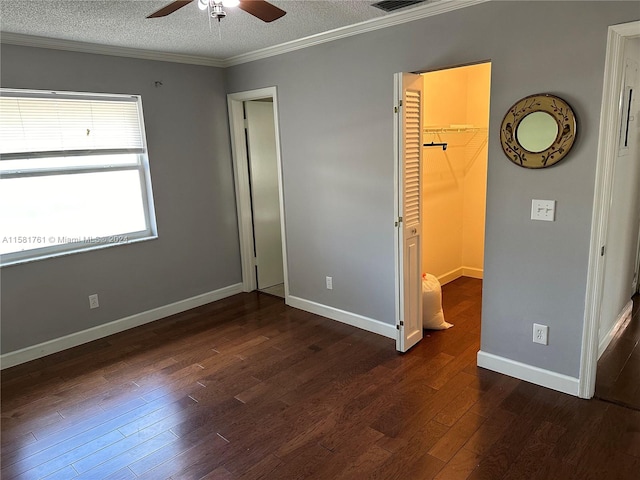 unfurnished bedroom featuring a spacious closet, ceiling fan, a textured ceiling, dark wood-type flooring, and a closet