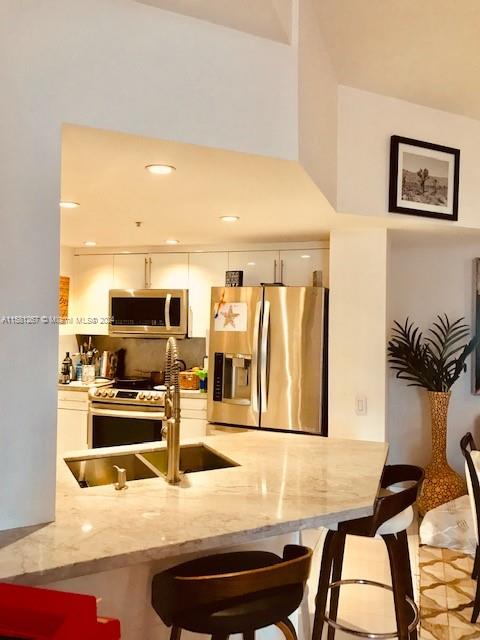 kitchen featuring white cabinetry, appliances with stainless steel finishes, a breakfast bar area, light stone counters, and sink