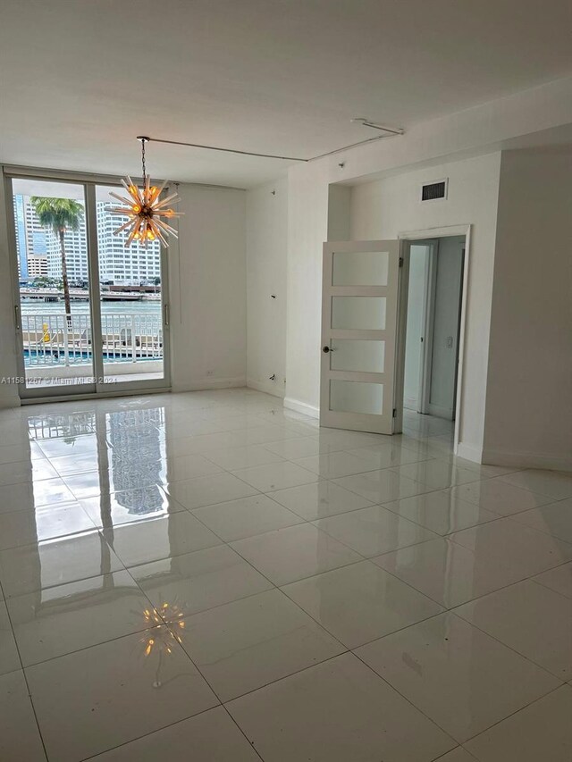 spare room with a chandelier, expansive windows, and light tile floors