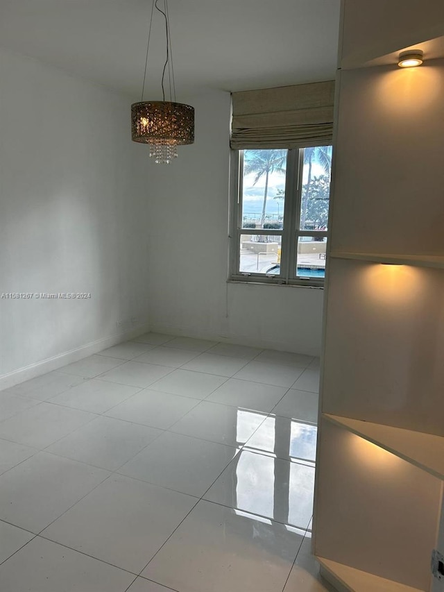 tiled empty room featuring an inviting chandelier