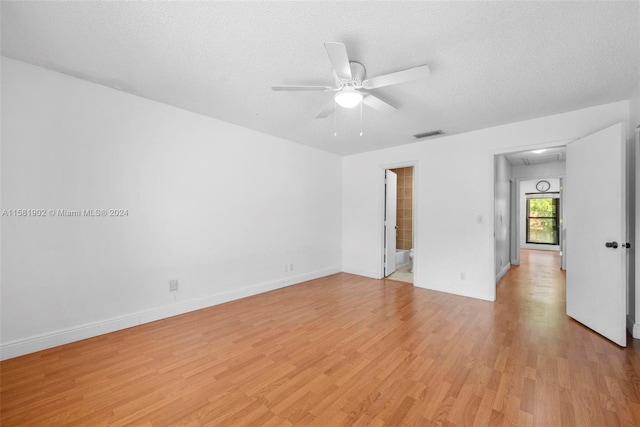 unfurnished room with light wood finished floors, visible vents, a ceiling fan, attic access, and a textured ceiling