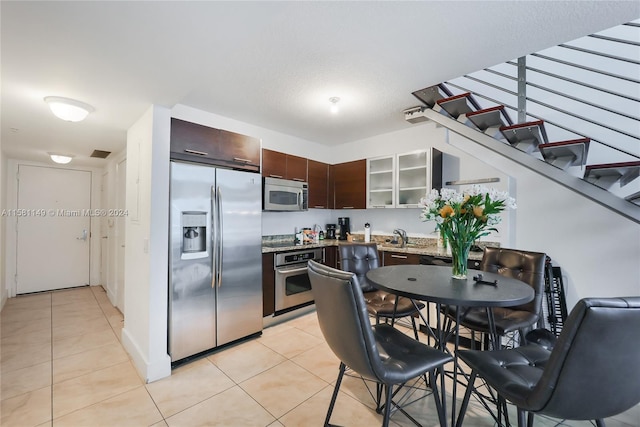 kitchen with appliances with stainless steel finishes, sink, dark brown cabinets, and light tile floors