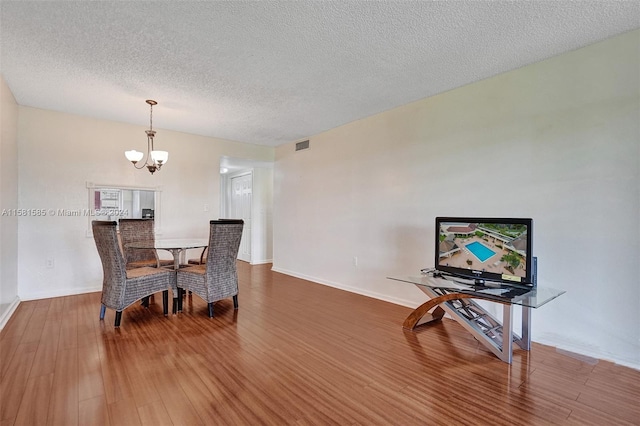 dining room with a textured ceiling, hardwood / wood-style floors, and an inviting chandelier