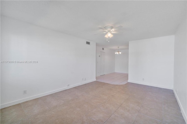 tiled empty room with ceiling fan with notable chandelier