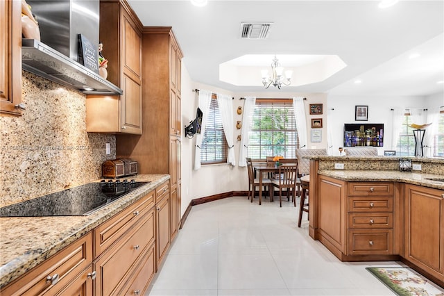 kitchen with black electric stovetop, wall chimney exhaust hood, light stone countertops, light tile patterned floors, and a raised ceiling