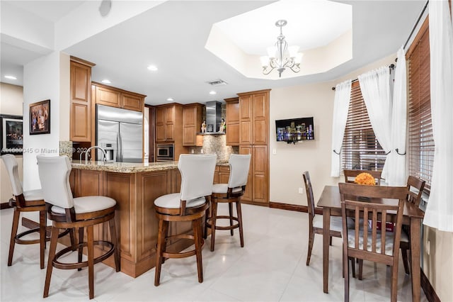 kitchen with kitchen peninsula, light stone counters, light tile patterned floors, a tray ceiling, and built in appliances