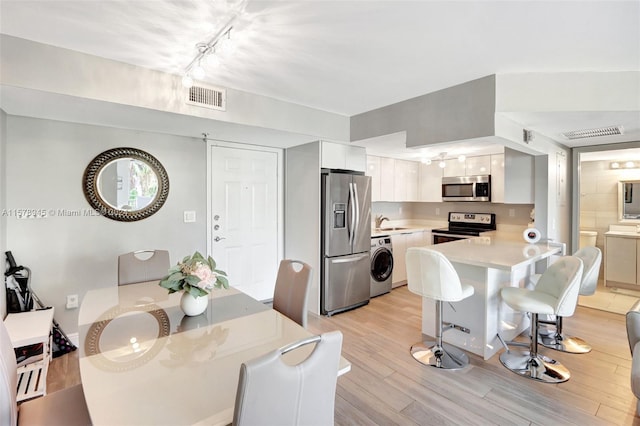 dining area featuring light wood-type flooring, rail lighting, sink, and washer / dryer