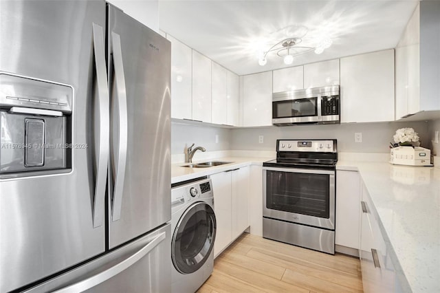 kitchen with appliances with stainless steel finishes, light hardwood / wood-style flooring, washer / clothes dryer, white cabinetry, and sink