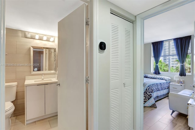 interior space with tile walls, vanity, toilet, and tile flooring