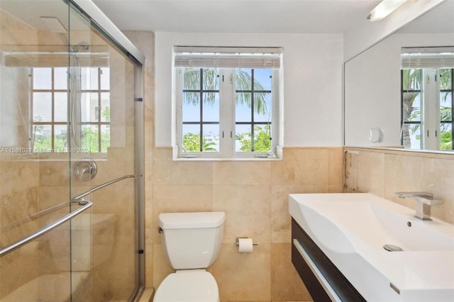 bathroom with tile walls, a shower with door, vanity, and toilet