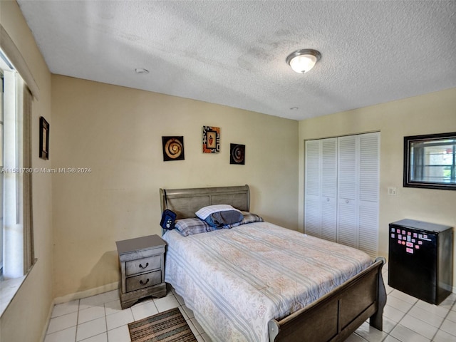 bedroom with a closet, a textured ceiling, and light tile floors