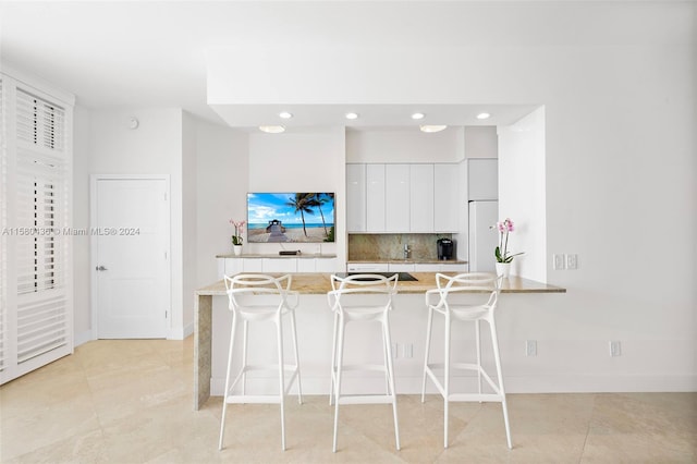 kitchen with tasteful backsplash, white cabinetry, light tile floors, and light stone countertops