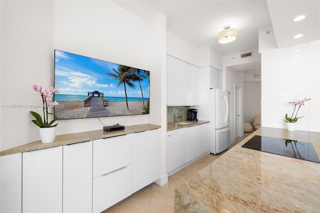 kitchen featuring white fridge, backsplash, light tile flooring, white cabinetry, and sink