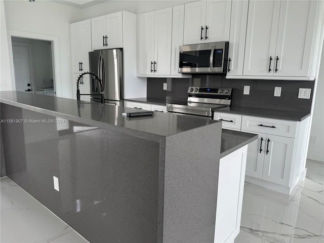 kitchen with a kitchen island with sink, stainless steel appliances, white cabinetry, and light tile flooring